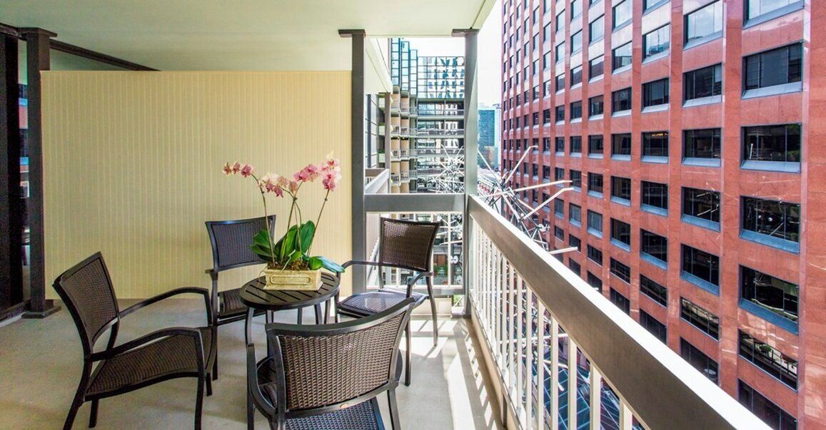 Un balcon avec une table et des chaises, un pot de fleurs et une vue sur un immeuble rouge doté de nombreuses fenêtres.