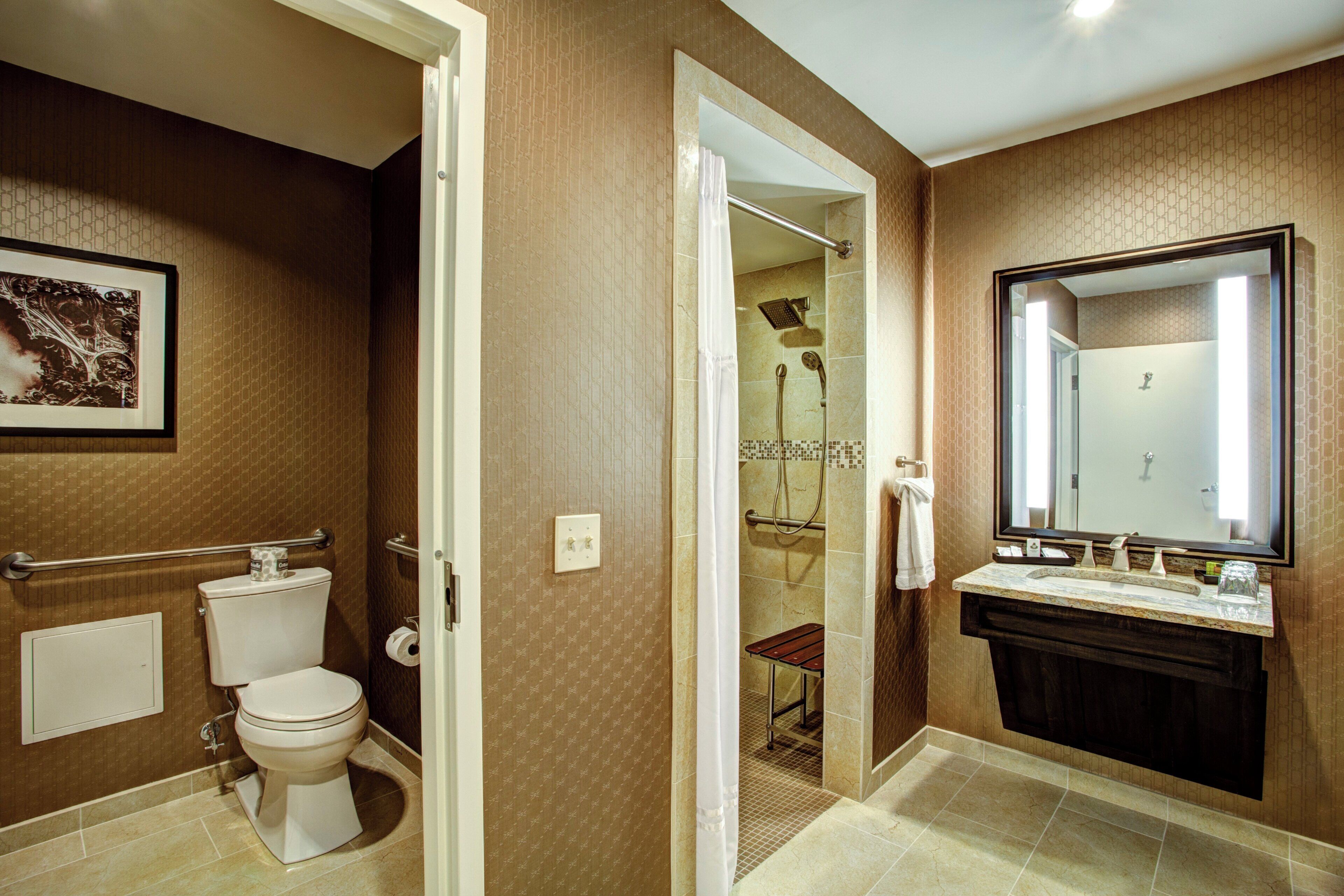 A bathroom with a toilet, a sink with a mirror, and a shower area.