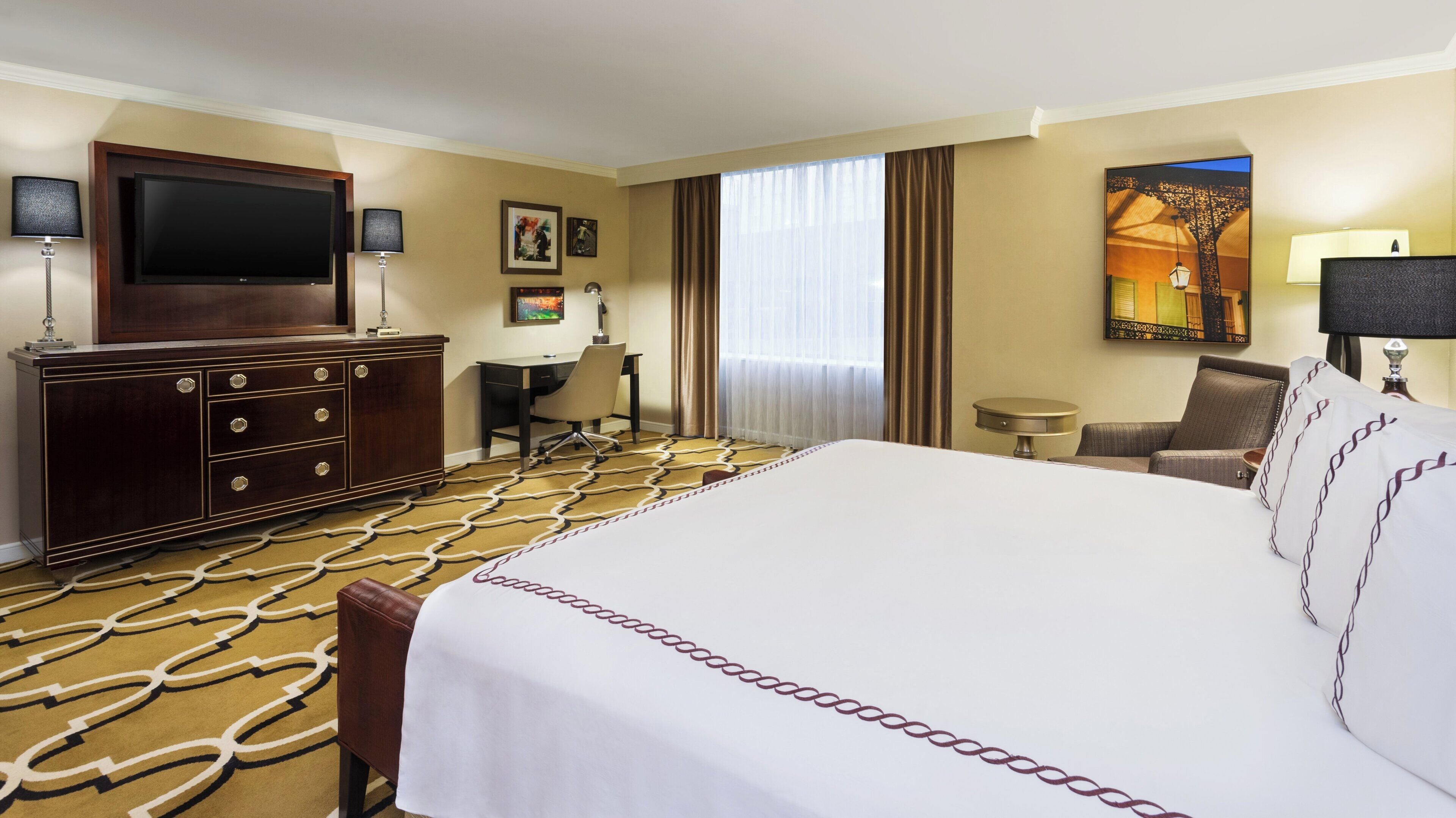 A hotel room with a large bed, a desk, a television, a chair, and a painting on the wall.