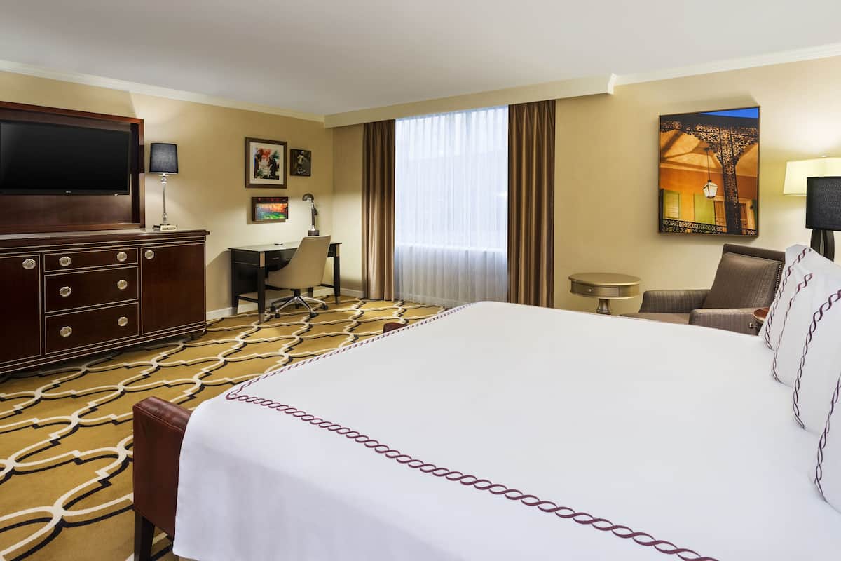 A hotel room with a large bed, a desk, a chair, a television, and a painting on the wall.