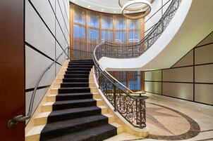 A grand staircase with a curved design, featuring a black and beige carpeted floor and ornate metal railings.