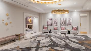 Un vestíbulo amplio con una lámpara moderna, una alfombra estampada y una zona de recepción con asientos y obras de arte.