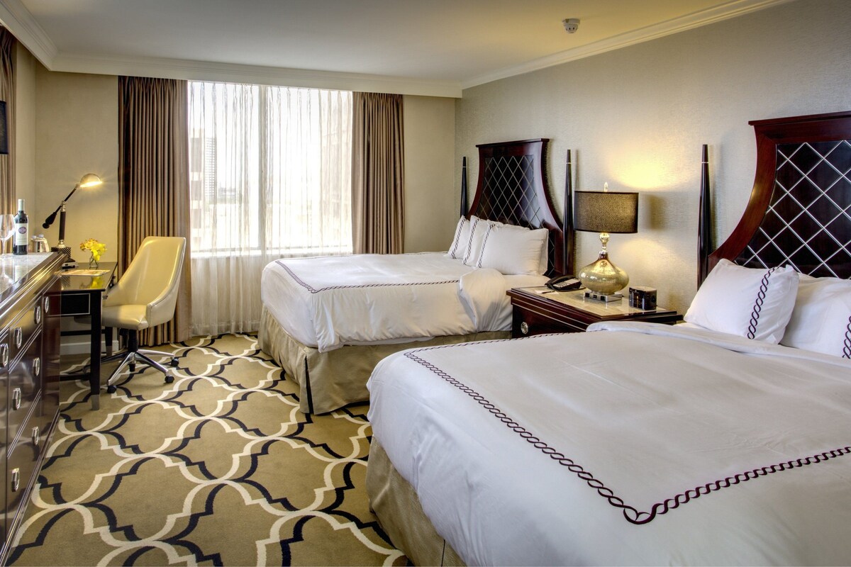 A hotel room with two beds, a desk with a computer, a chair, and a TV.
