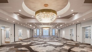 Un'ampia hall d'albergo con un grande lampadario, una moquette decorata e diverse porte che conducono alle camere.