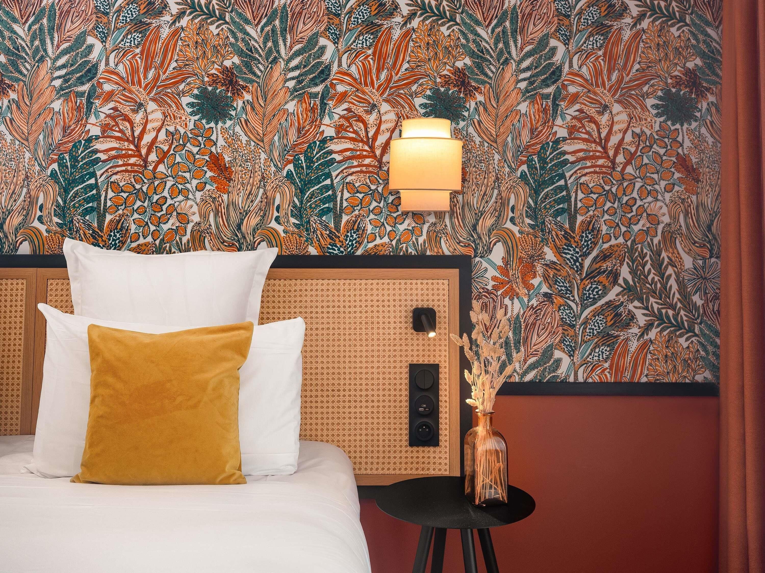 Quarto de hotel com cama, mesa de cabeceira, luminária de parede e um vaso decorativo.