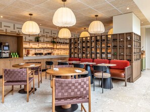 Een modern interieur met ronde tafels, beklede zitplaatsen, hanglampen en een wand vol camera's.