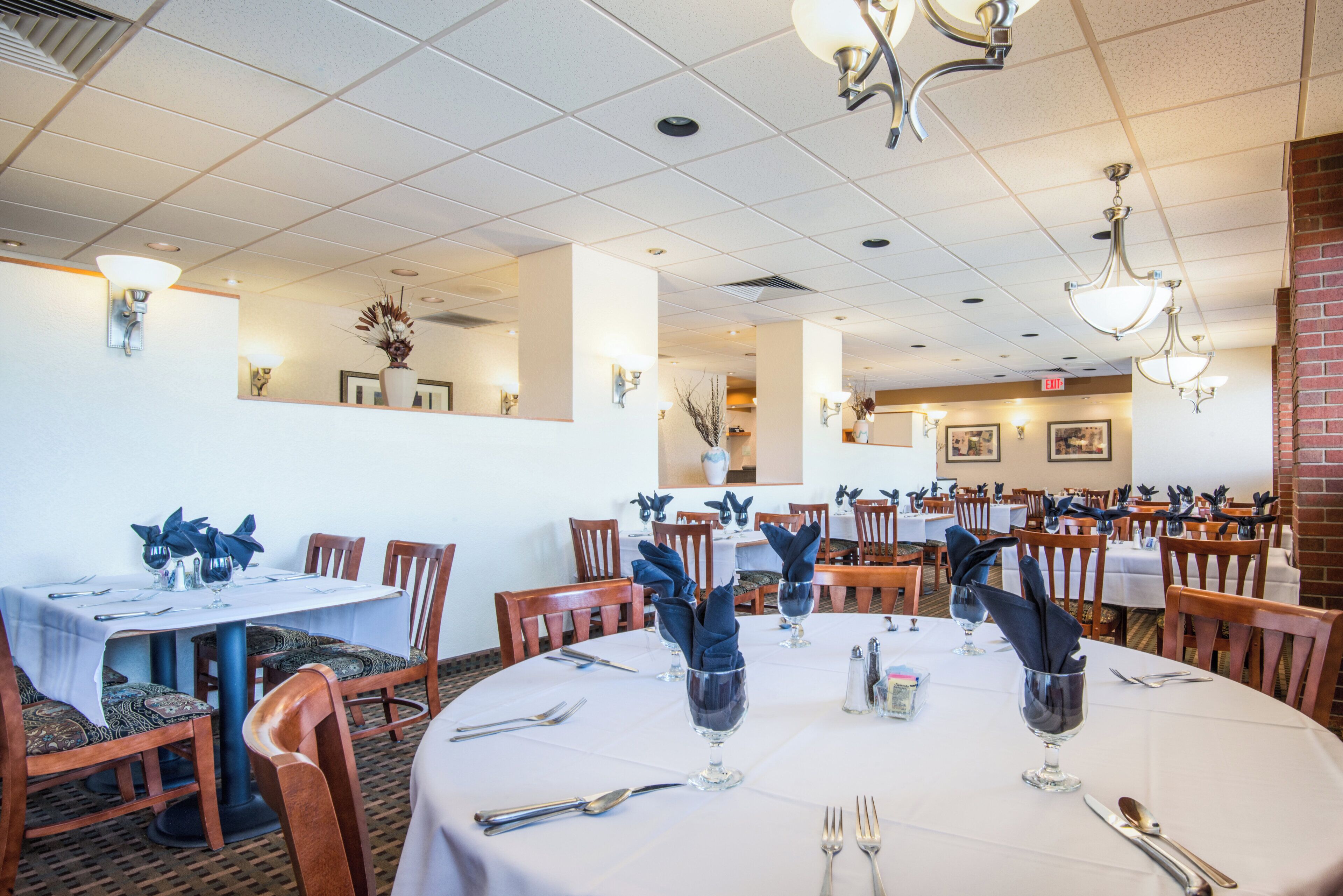Un restaurant doté de nombreuses tables dressées pour le service, avec une variété de chaises et un plafond équipé d’un éclairage encastré.