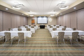 Une salle de conférence équipée de plusieurs tables et chaises, d’un écran de projection et d’un panneau indiquant la sortie.