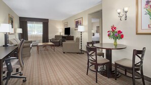 A hotel room with a sofa, armchairs, a dining table with chairs, a TV, and a vase of flowers. - Holiday Inn Riverton by IHG (Riverton)