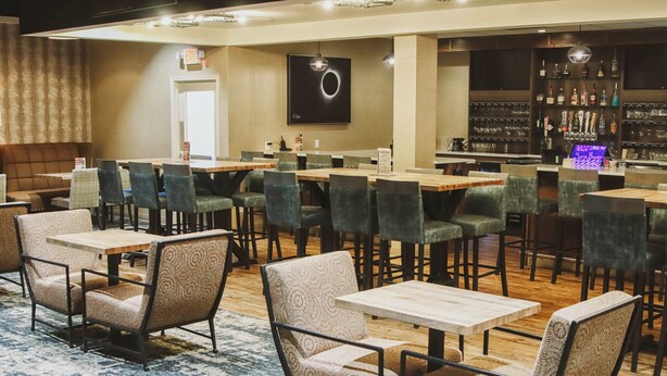 A restaurant with multiple tables and chairs, a bar area with bottles and glasses, and a sign indicating the exit. - Holiday Inn Riverton by IHG (Riverton)