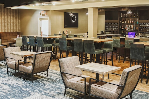 A restaurant with multiple tables and chairs, a bar area with bottles and glasses, and a sign indicating the exit. - Holiday Inn Riverton by IHG (Riverton)
