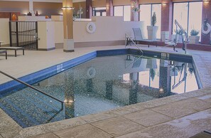 A swimming pool with a tiled deck, a lounge area with chairs and a table, and a brick wall with windows. - Holiday Inn Riverton by IHG (Riverton)