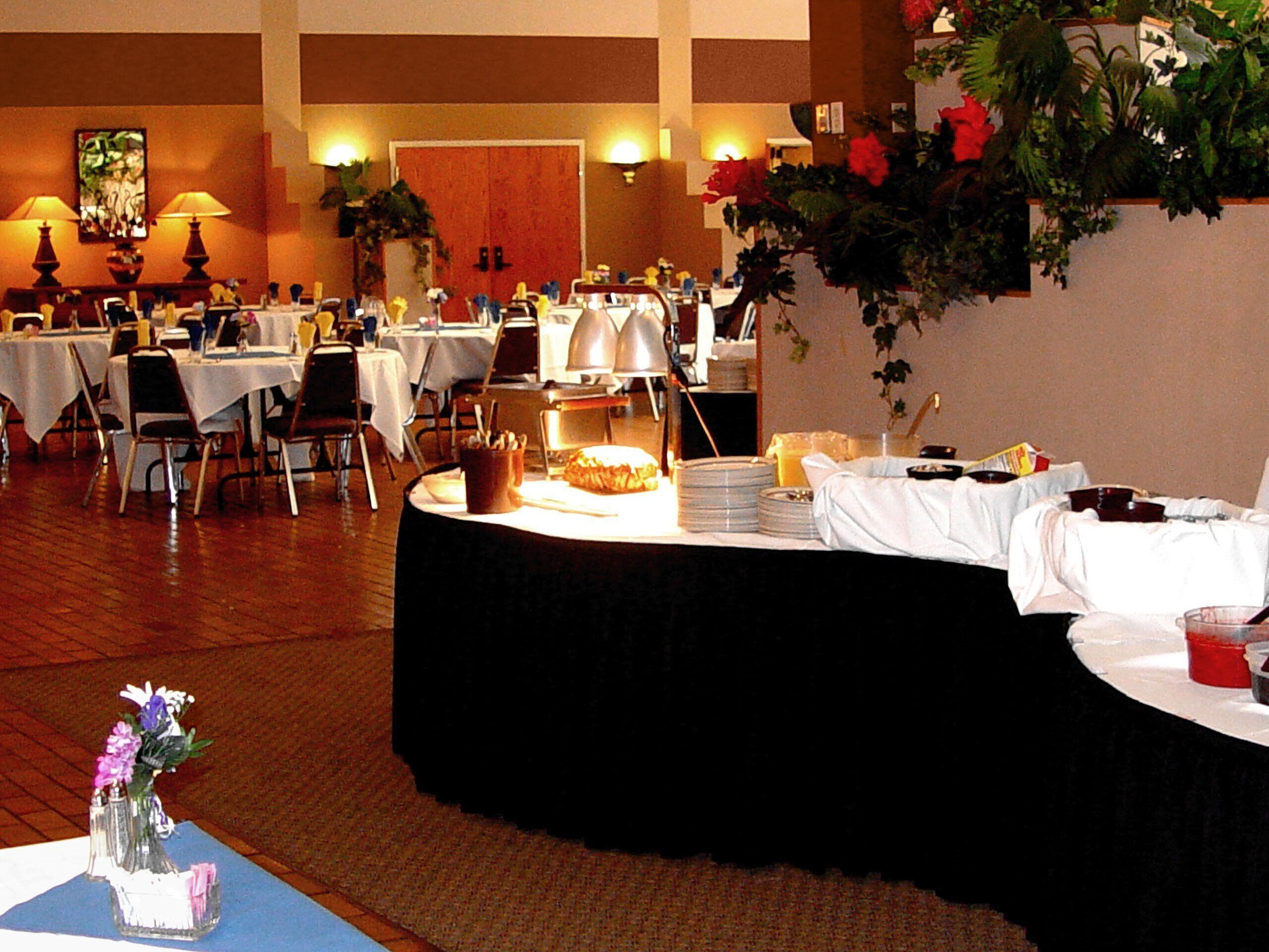Un salón de banquetes con mesas redondas, sillas y una barra de buffet.