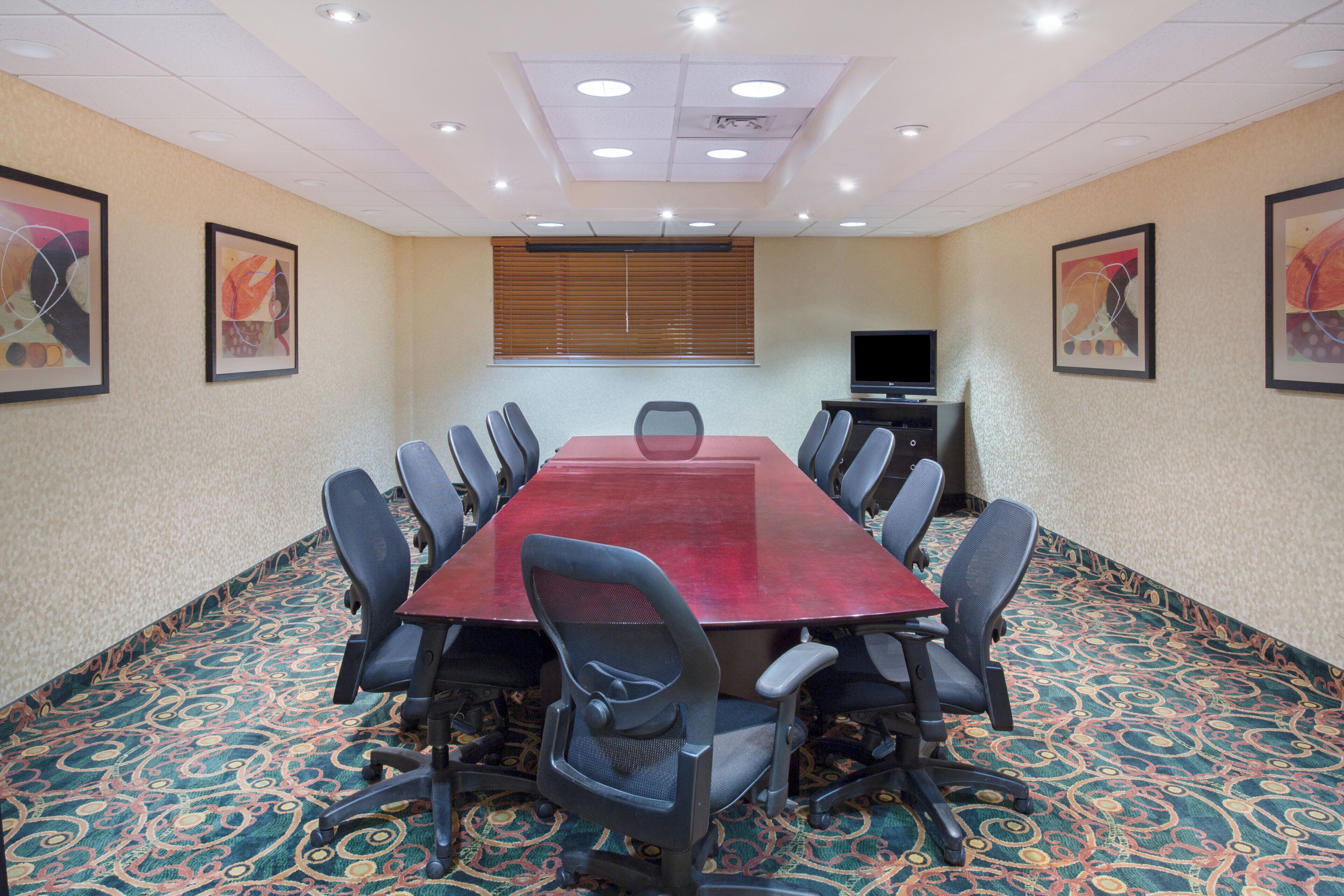 Une salle de conférence avec une longue table, des chaises, un téléviseur et des œuvres d’art encadrées accrochées aux murs.