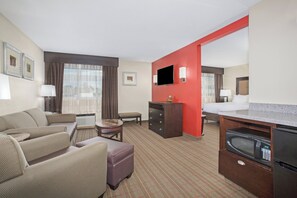 A hotel room with a living area, a bed, a kitchenette, and a television. - Holiday Inn Riverton by IHG (Riverton)