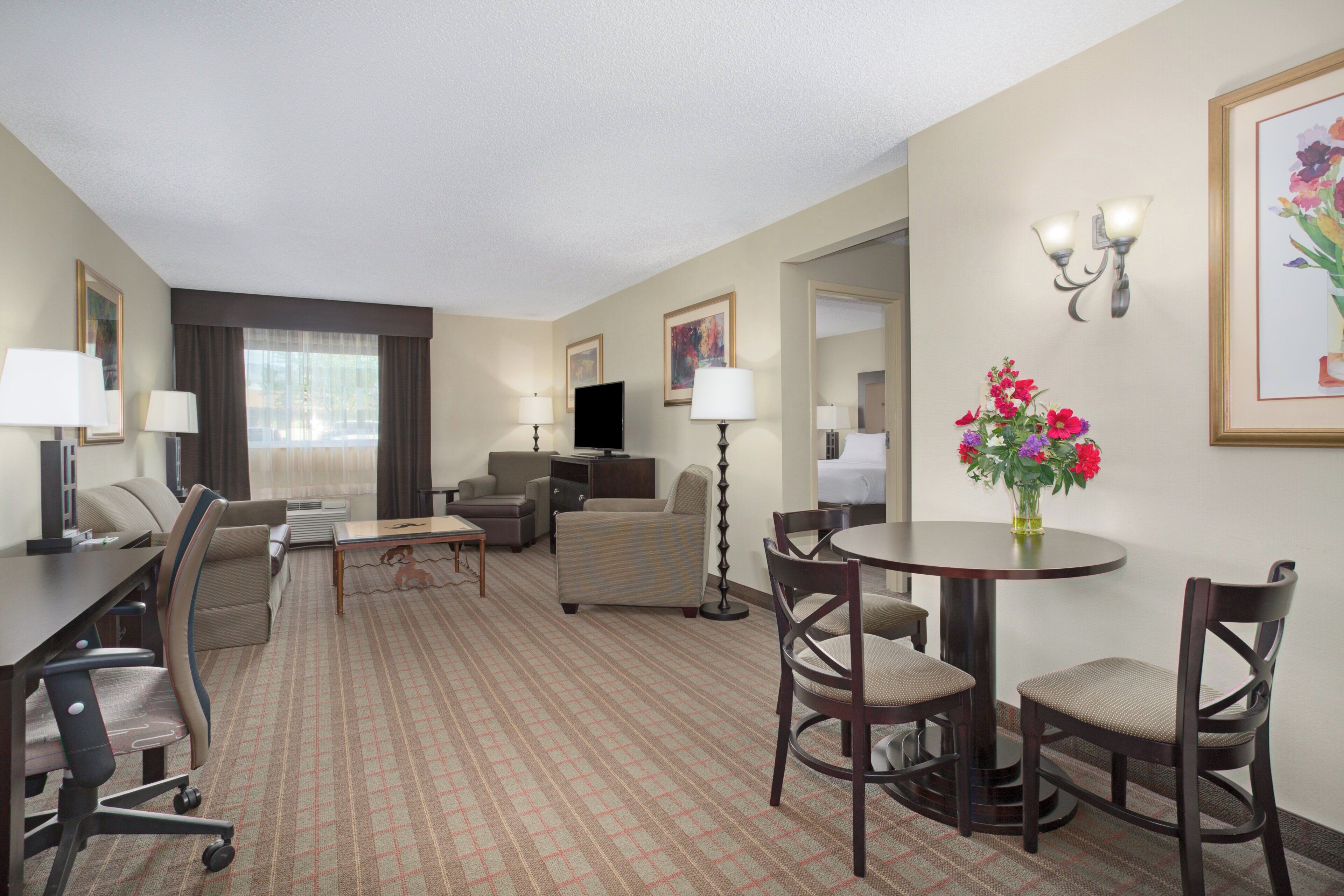 Une chambre d’hôtel comprenant un coin repas, un canapé, une télévision et une grande fenêtre avec des rideaux.