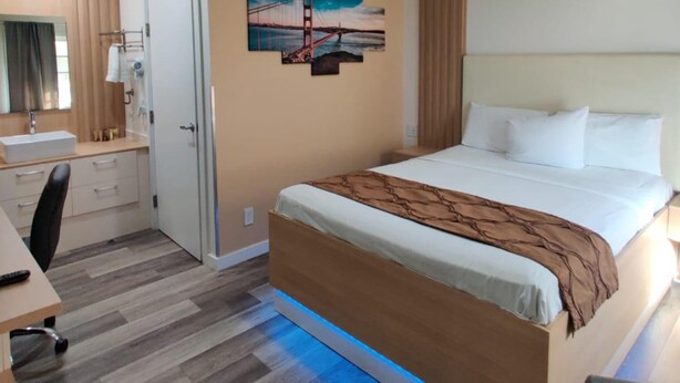 A hotel room with a bed, bedside table, desk, chair, and a painting of a bridge. - San Francisco Inn (San Francisco)
