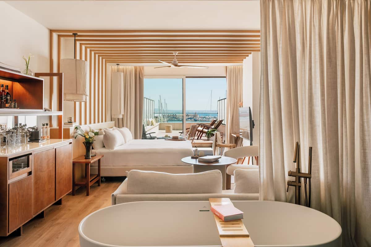 Una habitación de hotel moderna con balcón, zona de comedor y vistas al puerto deportivo.