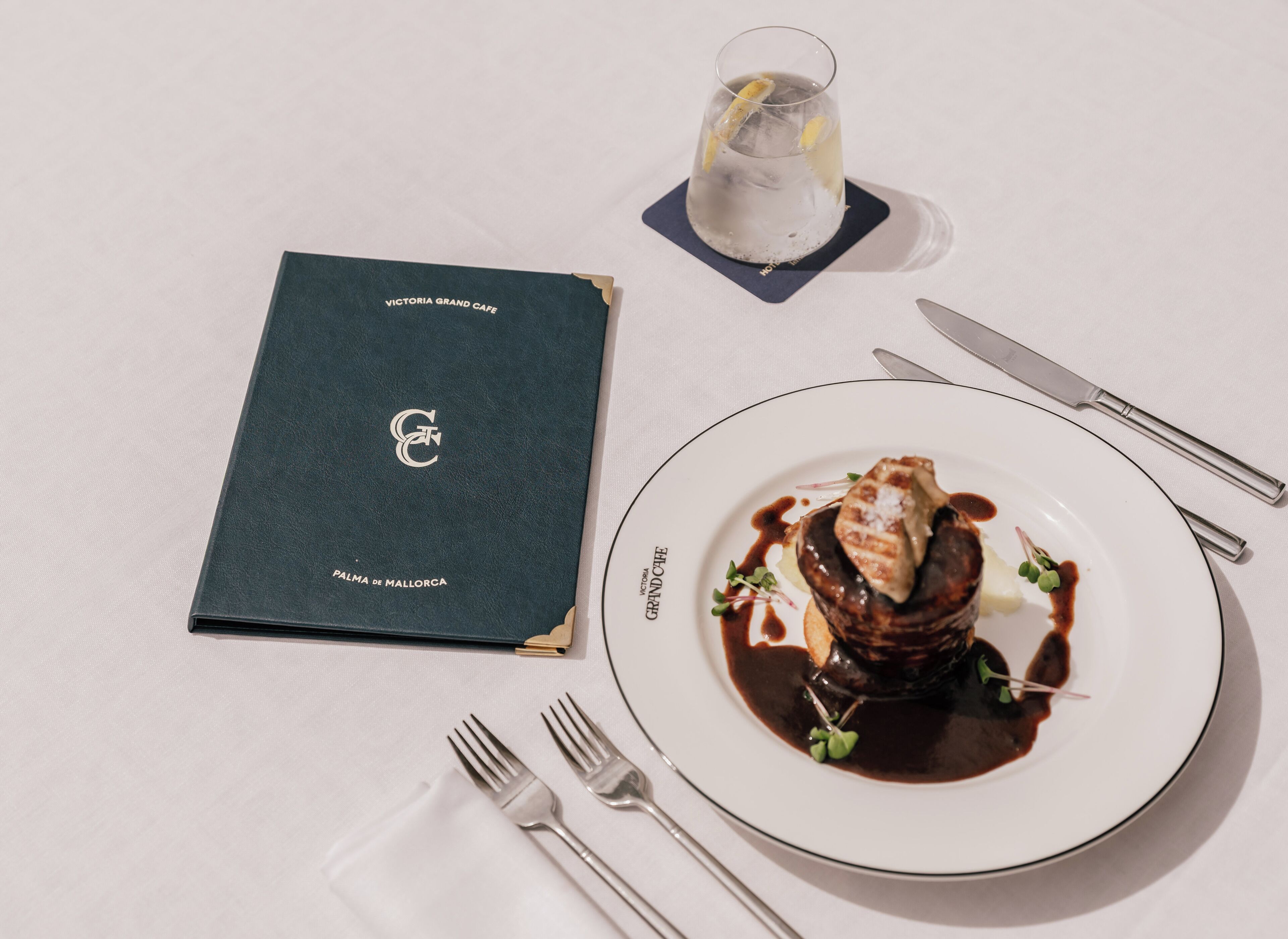 A formal dining setup with a menu, a glass of water, and a plate of food.