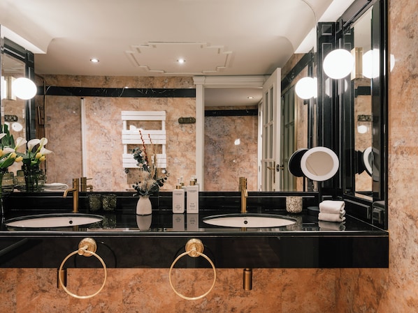 Une salle de bain moderne avec deux vasques, des plans de toilette en marbre, des robinetteries dorées et un grand miroir avec éclairage intégré.