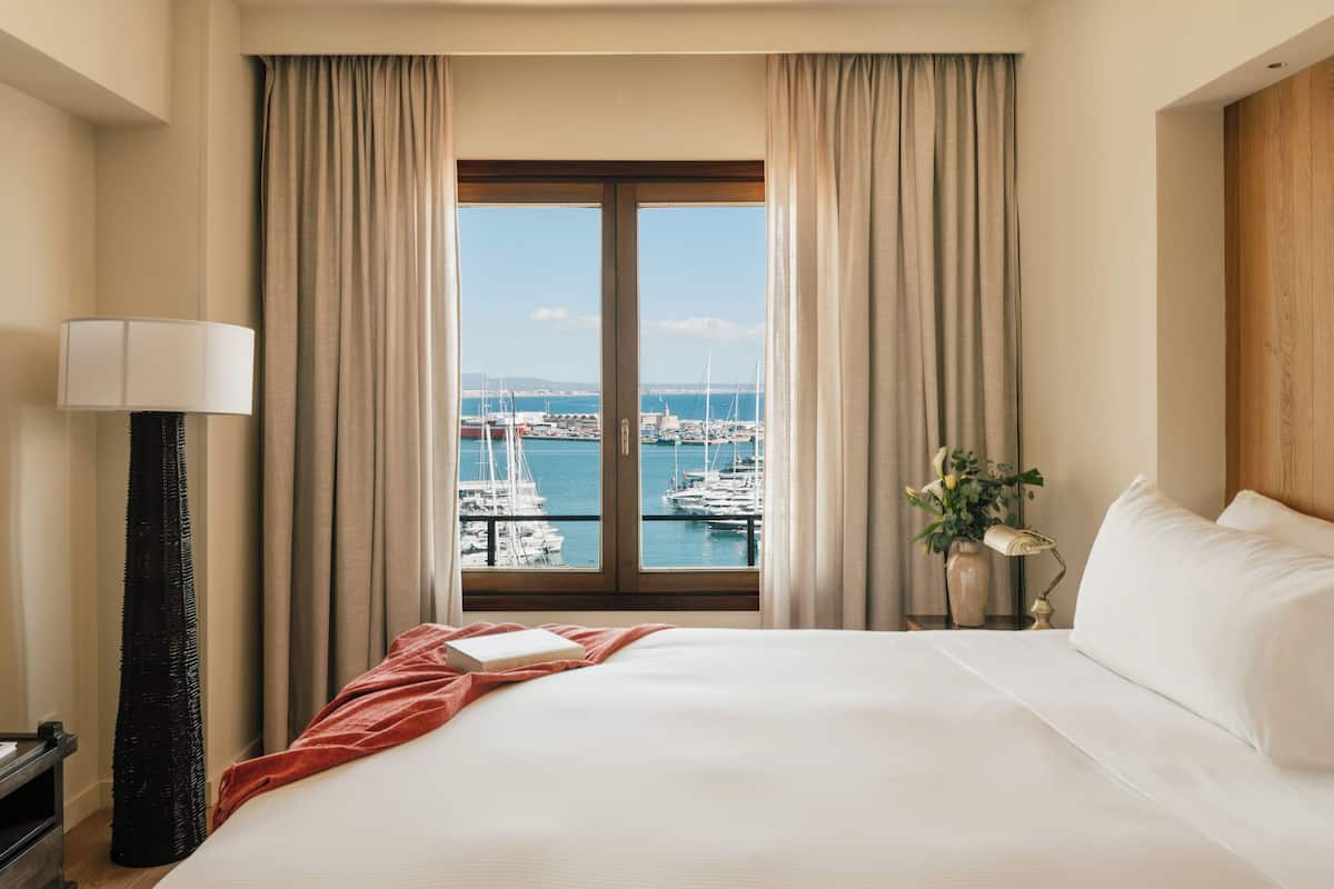 Habitación de hotel con una cama grande, vistas a un puerto deportivo y una lámpara.