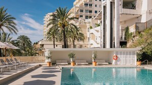 A swimming pool with lounge chairs and palm trees, surrounded by a multi-story building with balconies. - Hotel Victoria Gran Meliá (Palma de Mallorca)