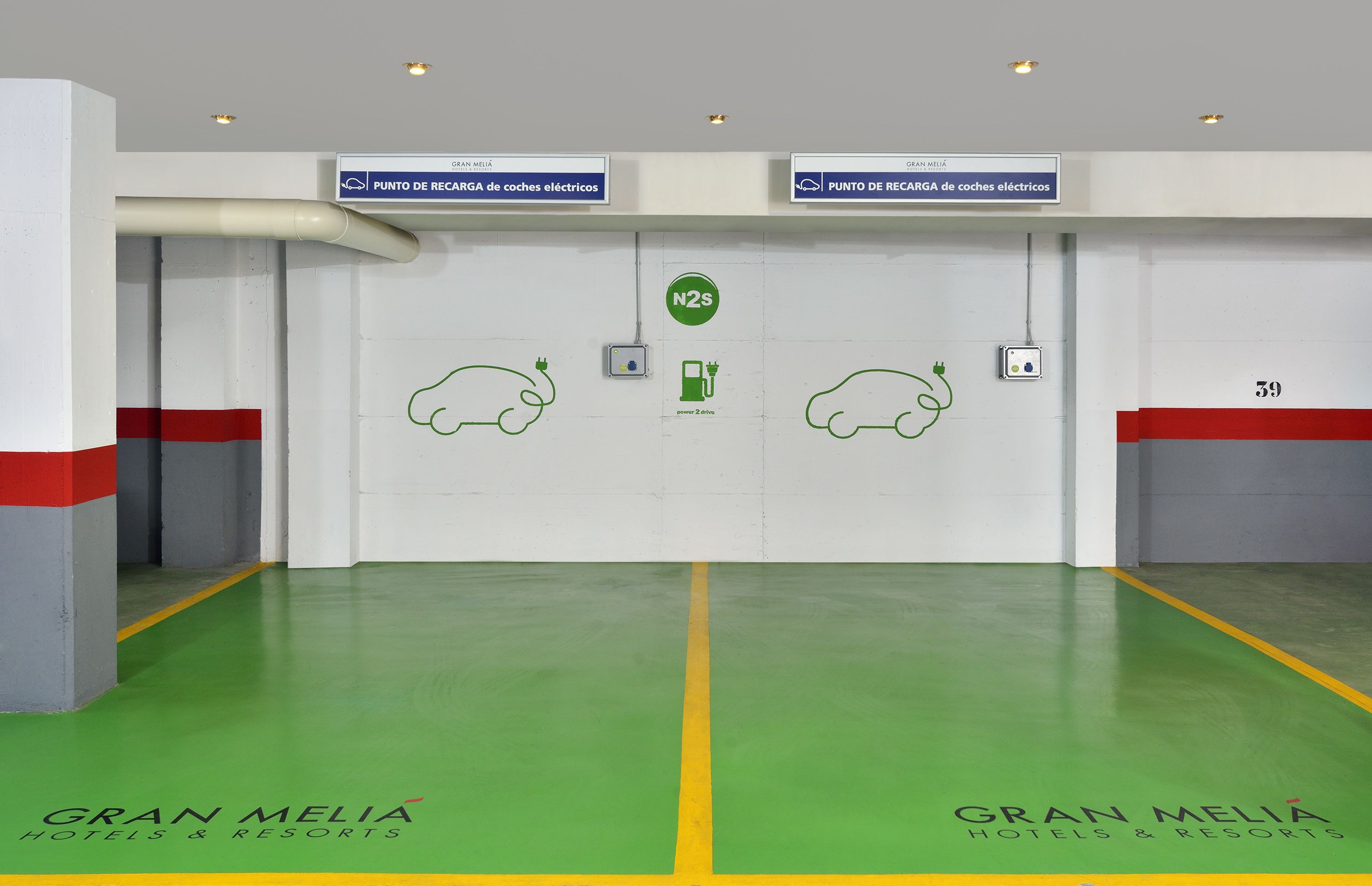 A clean, modern hotel lobby with green flooring, white walls, and red accents. There are signs indicating electric car charging points and a N2S charging station.