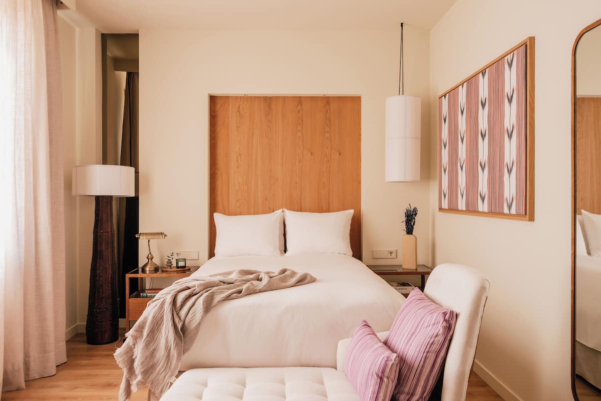 Una habitación de hotel moderna con una cama grande, mesitas de noche, una lámpara y un espejo.
