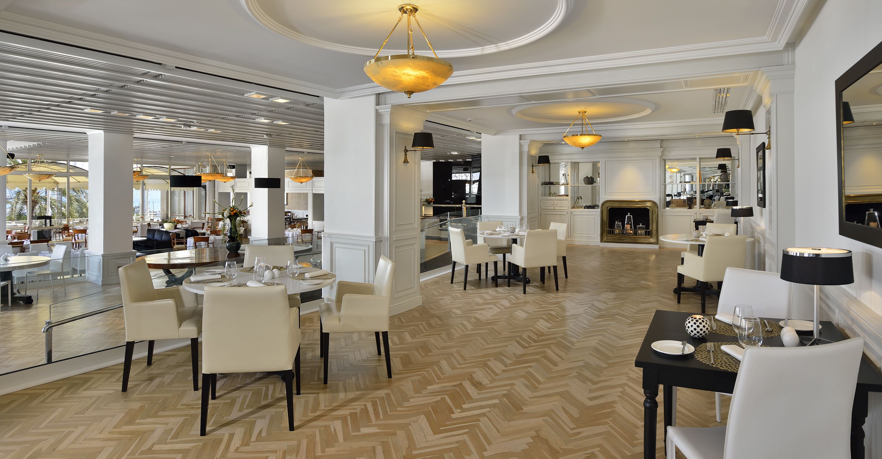 A spacious dining area with high ceilings, modern chandeliers, and a herringbone wood floor.