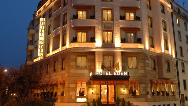 Un hotel de varios pisos con un cartel llamativo que dice "HOTEL EDEN". El edificio tiene balcones en cada planta y la entrada está iluminada.