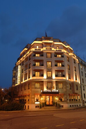 Un hotel de varios pisos con un cartel llamativo que dice "HOTEL EDEN". El edificio tiene balcones en cada planta y la entrada está iluminada.
