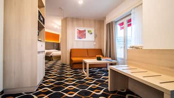 Ett modernt hotellrum med ett mönstrat golv, en soffa, ett litet bord med en vas, ett skrivbord i trä och en säng i bakgrunden.