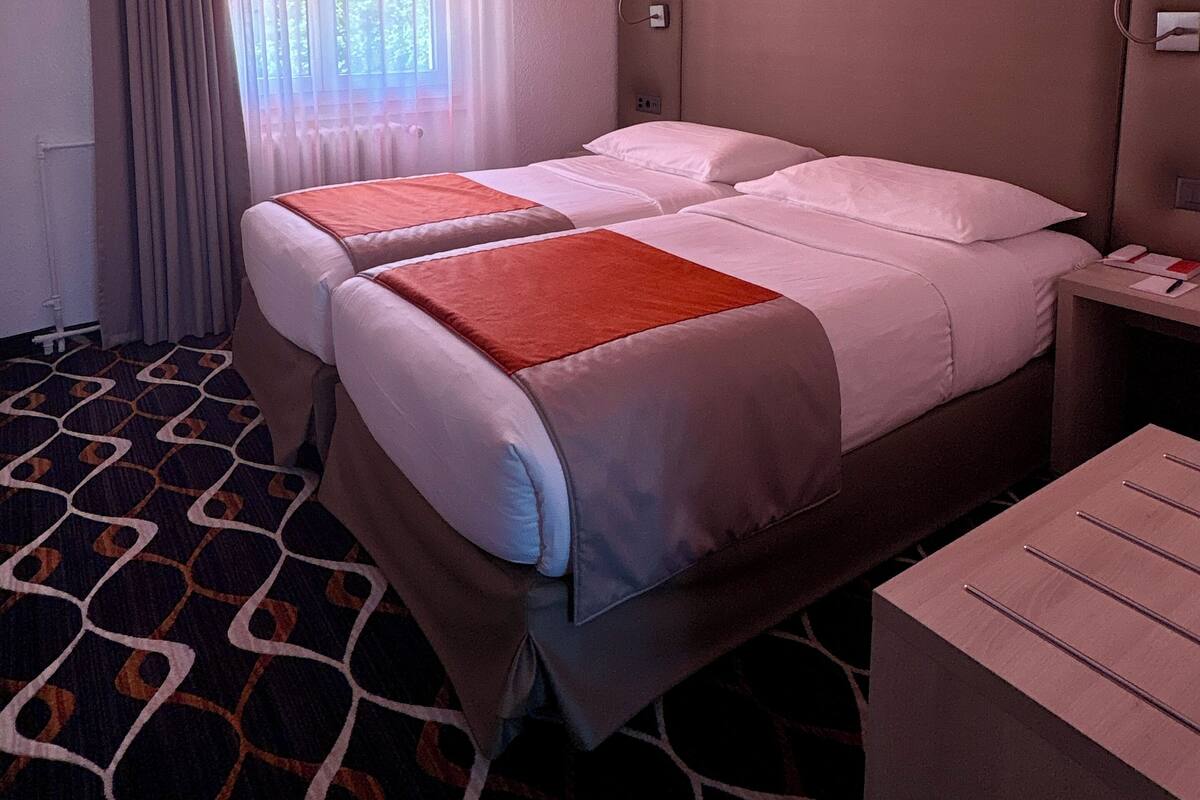 A hotel room with two beds, a nightstand, a desk, and a patterned carpet.