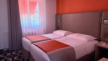 A hotel room with two beds, a nightstand, a desk, and a patterned carpet.
