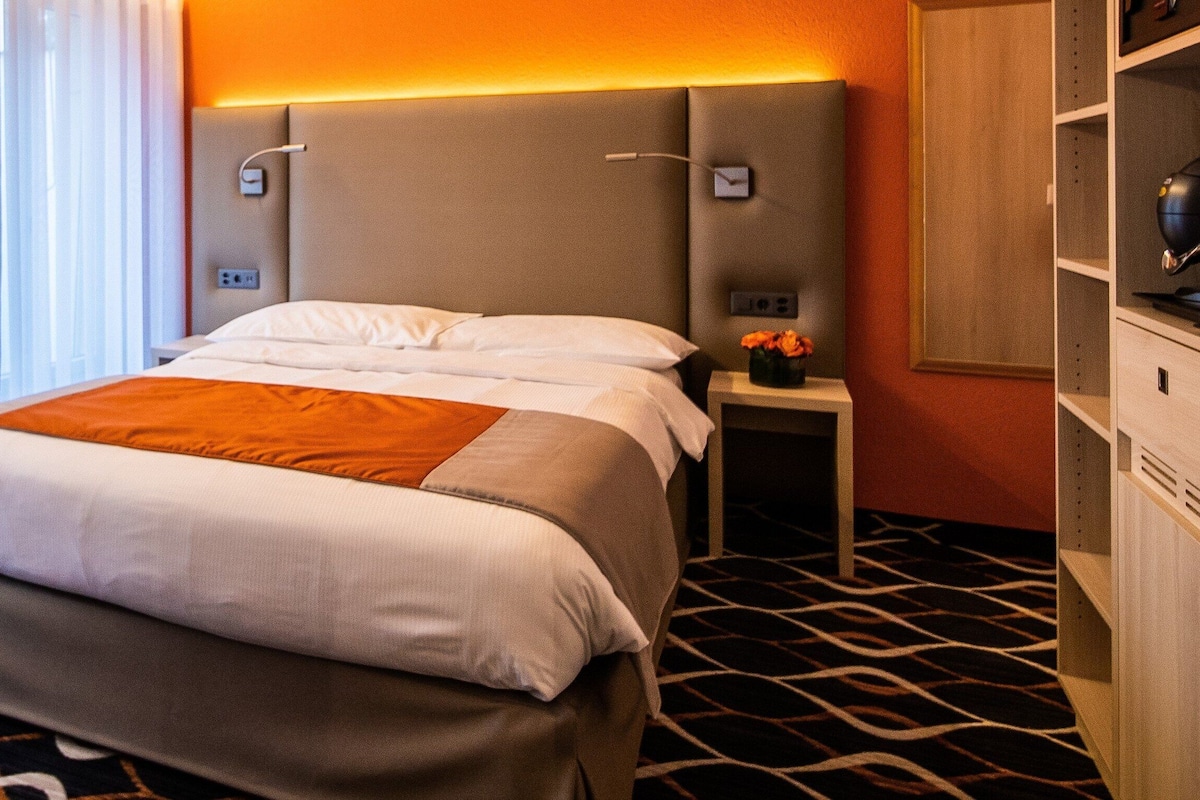 A hotel room with a bed, a desk, a chair, a nightstand, and a lamp.