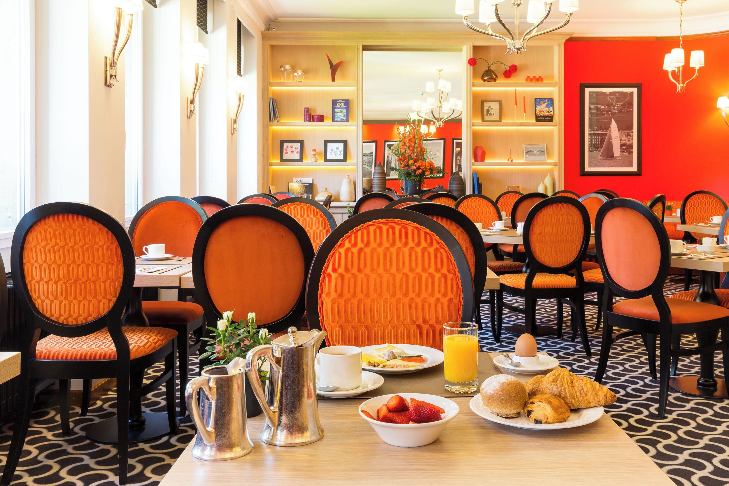 Un coin repas avec des chaises à revêtement orange, une table où sont disposés des aliments pour le petit-déjeuner et un sol à motifs.