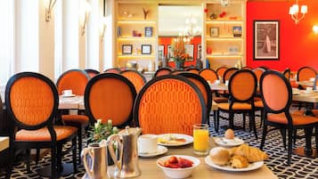 Un coin repas avec des chaises à revêtement orange, une table où sont disposés des aliments pour le petit-déjeuner et un sol à motifs.