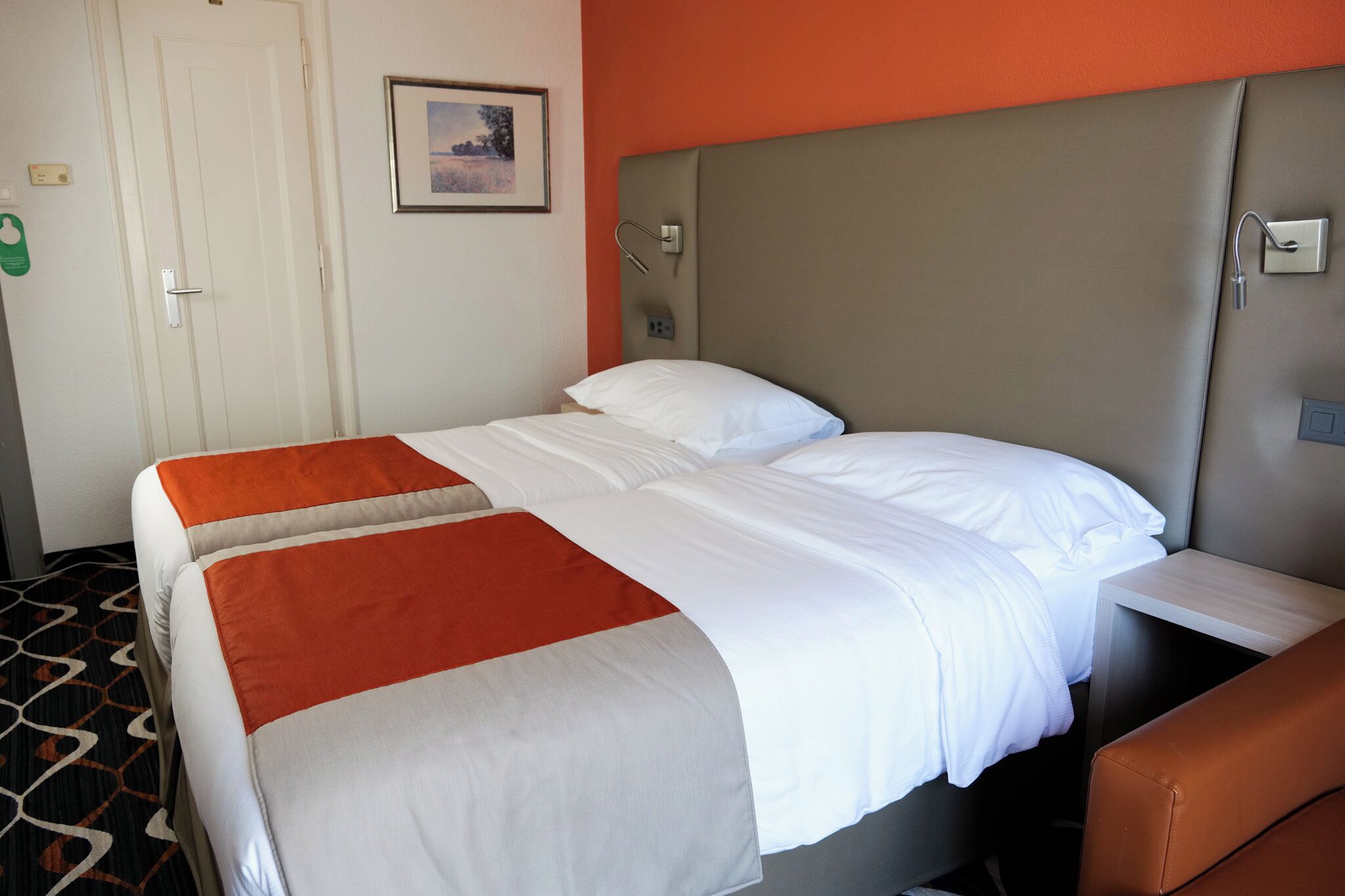 Une chambre d’hôtel avec deux lits, une tête de lit, une table de chevet et une chaise marron.