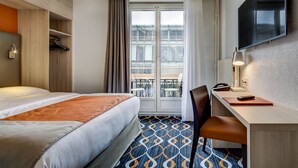 Habitación de hotel con cama, escritorio, silla y televisor montado en la pared.