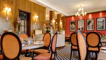 Ein Restaurant mit runden Tischen, gepolsterten Stühlen und einem gemusterten Boden.