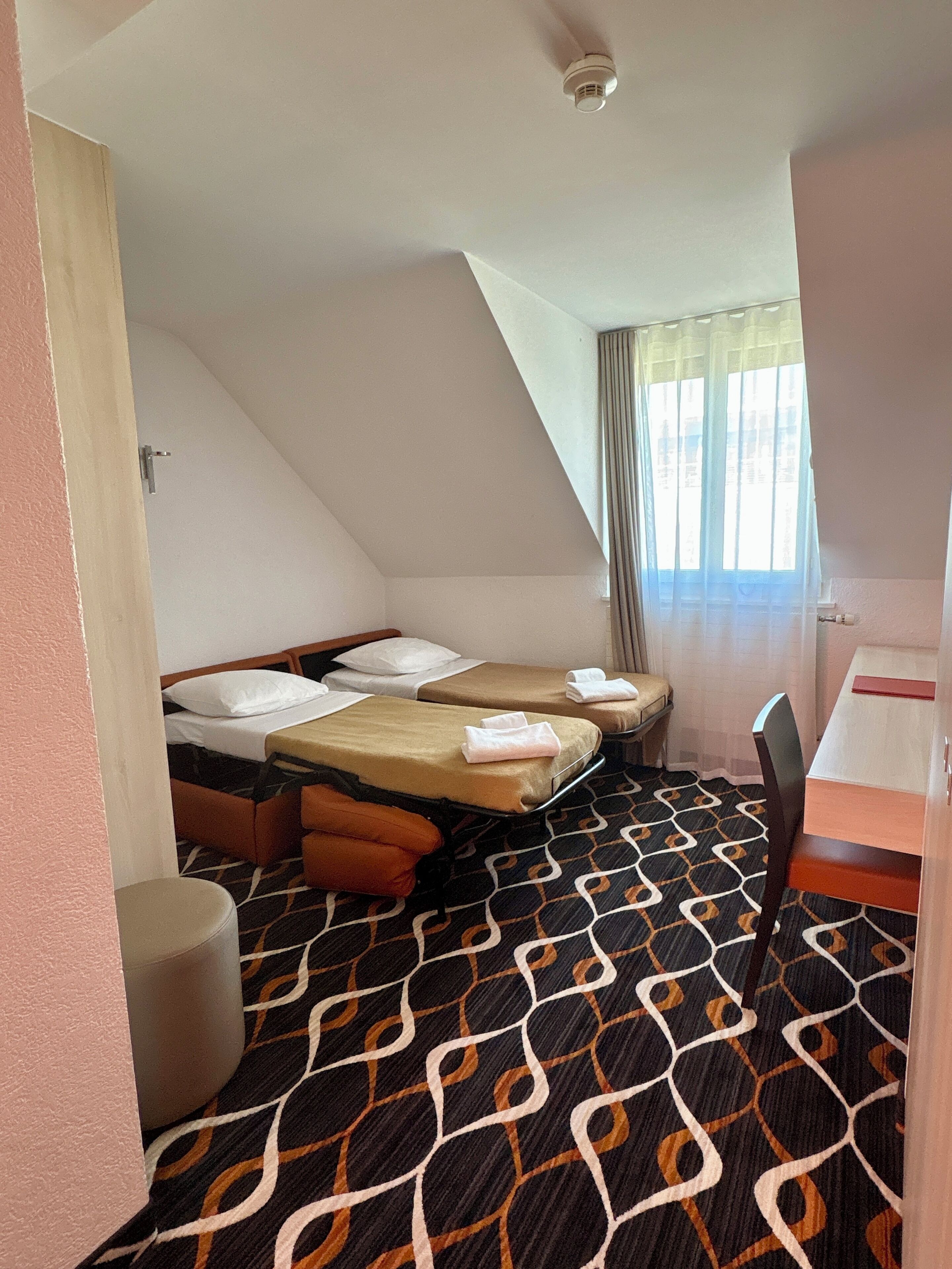 Quarto de hotel com duas camas, uma mesa pequena e uma cadeira.