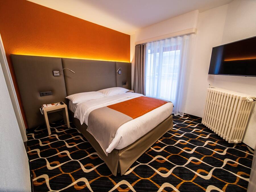 Une chambre d’hôtel avec un lit, une table de chevet, une télévision et une fenêtre avec des rideaux.