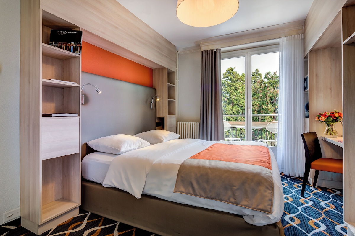Hotellihuone, jossa on sänky, työpöytä, tuoli, kirjahylly ja näkymä ulos.