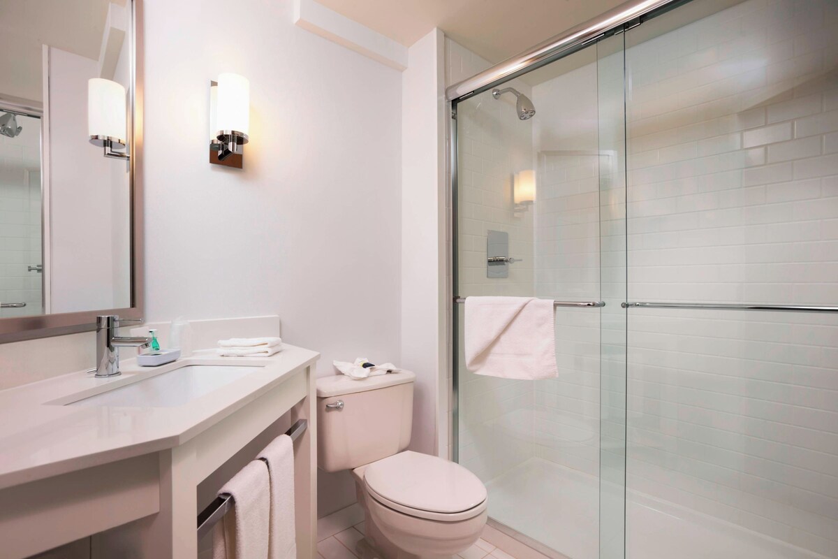 Een moderne badkamer met een douchecabine van glas, een wit toilet en een wastafel met spiegel en verlichting.
