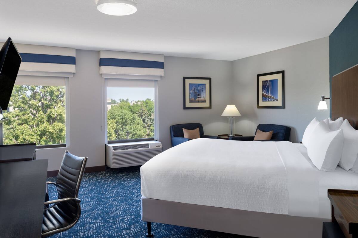 A hotel room with a large bed, a desk, a chair, two bedside tables, a lamp, and two framed pictures on the wall.