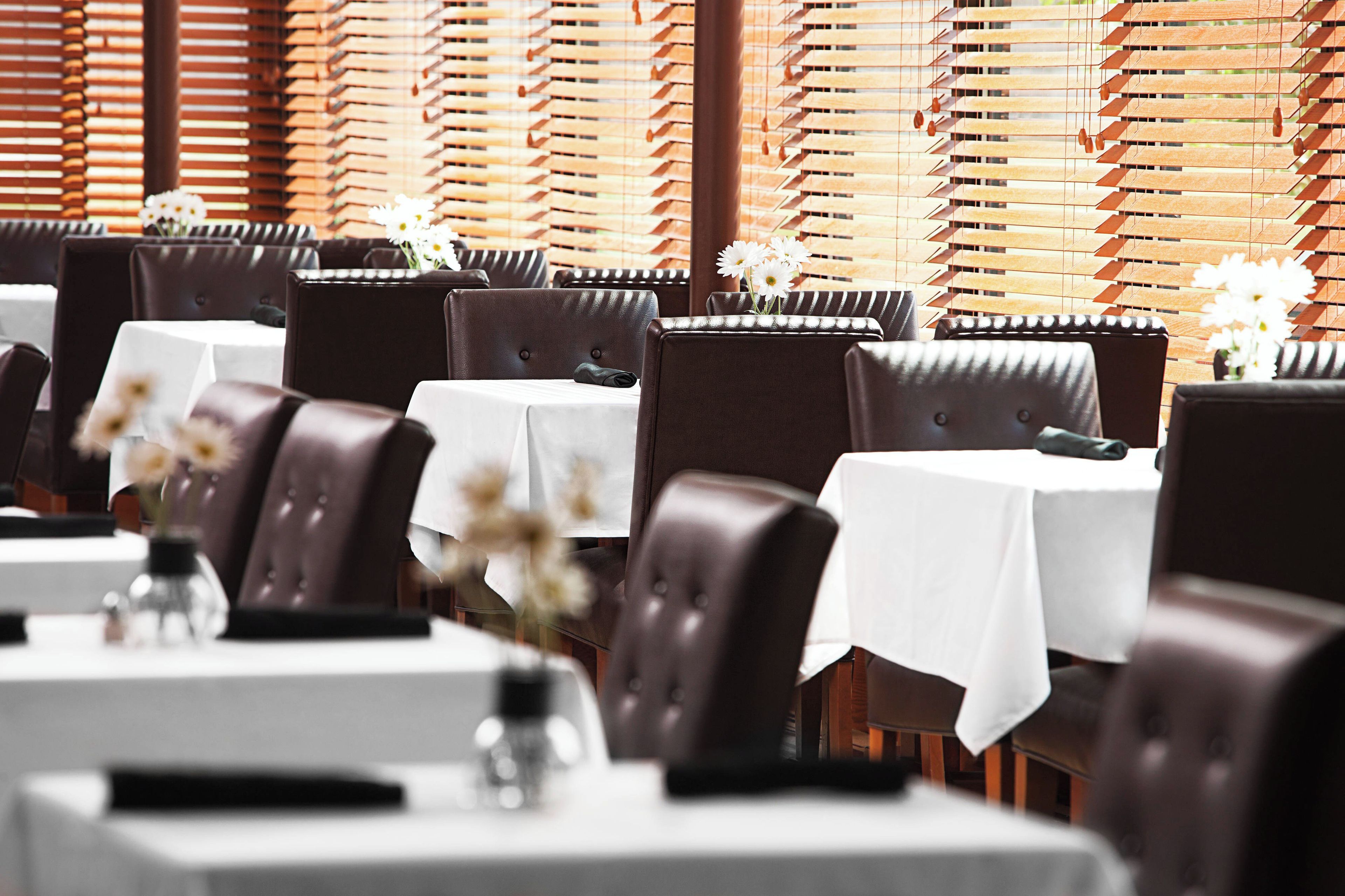 Un interior de restaurante con varias mesas y sillas, cada una con mantel blanco y un jarrón de flores.
