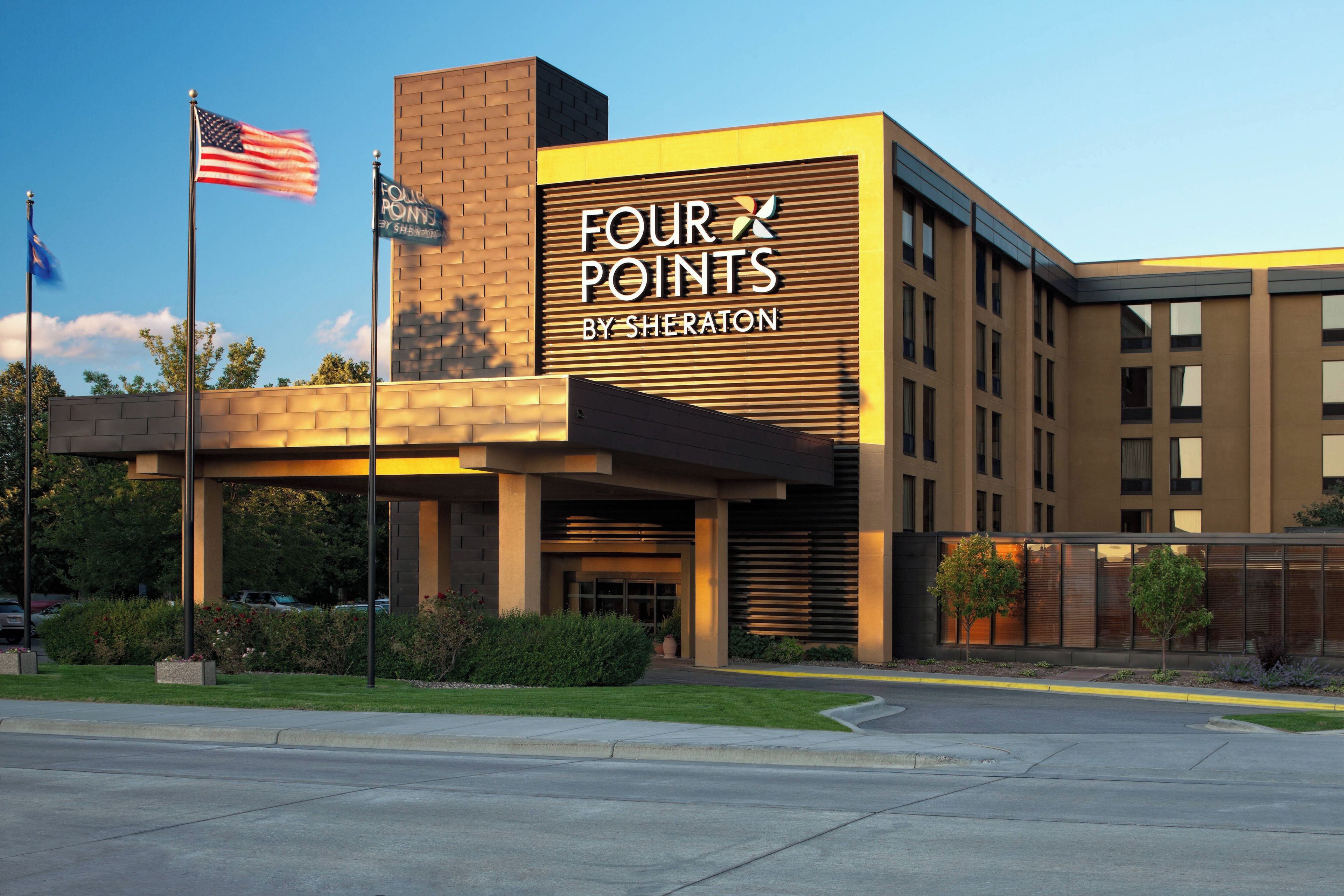 A hotel with a modern facade, a prominent sign reading 'FOUR POINTS BY SHERATON,' and a flagpole with an American flag.
