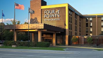A hotel with a modern facade, a prominent sign reading 'FOUR POINTS BY SHERATON,' and a flagpole with an American flag.
