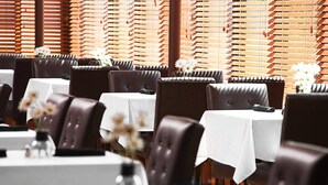 A restaurant with multiple tables and booths, each with a white tablecloth and brown leather chairs. - Four Points by Sheraton Mall of America Minneapolis Airport (Richfield)