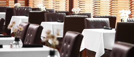 Ein Restaurant mit mehreren Tischen und Sitzecken, alle mit weißer Tischdecke und braunen Ledersesseln.